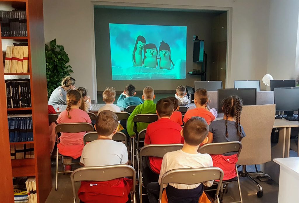 Uczniowie oglądają w Bibliotece fragment filmu animowanego "Pingwiny z Madagaskaru"