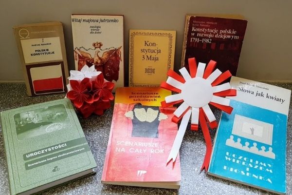 Książki poświęcone Konstytucji 3 Maja oraz biało-czerwone ozdoby - kotylion i kula kwiatowa
