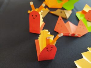 Czerwone ślimaki z żółtymi muszlami w kształcie harmonijki. W tle biedronki i jeżyki z origami.