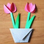 Dwa różowe tulipany z papieru w ekologicznej "doniczce" z szarej koperty. Prace plastyczne płaskie