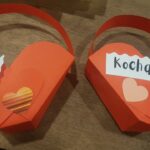 Dwa czerwone koszyczki z papieru, w kształcie serduszka, na prezent walentynkowy. Z przodu przyklejone napisy: LOVE i KOCHAM CIĘ