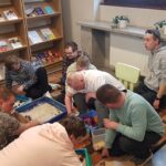 Uczestnicy warsztatów sandplay therapy podczas tworzenia obrazów w piaskownicach, które leża na dywanie.