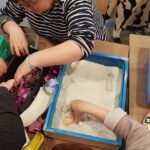 Uczestnicy warsztatów sandplay therapy tworzą w mini piaskownicach obrazy z muszelek, szyszek i kwiatów