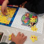 Dzieci układają puzzle. Na stoliku leżą też kredki