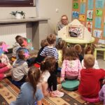 Przedszkolaki siedzą na dywanie i słuchają opowieści "Noc w bibliotece" z teatrzyku Kamishibai