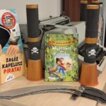 Na blacie obok maszyny do pisania stoją książki o piratach, a także dwie lunety z rolek po ręcznikach papierowych oraz dwie pirackie szable z tektury