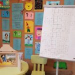 W sali bibliotecznej, na tle wystawy poświęconej bohaterom książeczek dla dzieci, stoi flipchart z krzyżówką, której hasłem jest "Dbam o zdrowie". Obok na stoliku stoi teatrzyk Kamishibai "W zdrowym ciele zdrowy duch"
