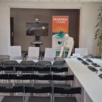 Sala biblioteczna z ułożonymi w rzędy krzesełkami, w tle telewizor, baner PBW i rzeźba czytającego mężczyzny oraz tablica informująca o Narodowym Czytaniu.